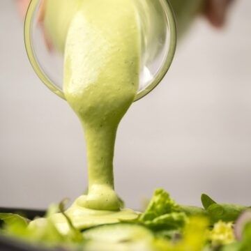Krämig grön dressing hälls över en sallad med bladgrönt